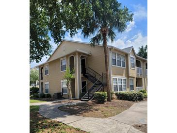 Tan two-story condo with exterior stairs, a palm tree, and a sidewalk at 1029 S Hiawassee Rd # 2414, Orlando, FL 32835