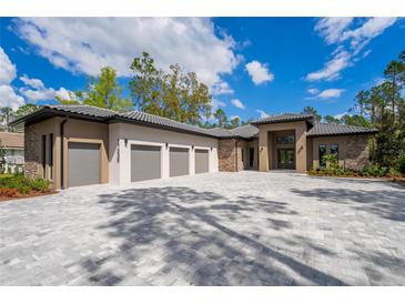 Stunning home featuring a three-car garage and elegant stone accents, set against a backdrop of blue skies and lush greenery at 17038 Medici Way, Bella Collina, FL 34756