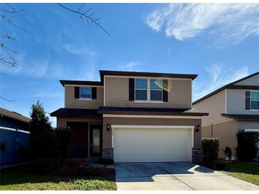 Two-story tan home with a two-car garage, well-manicured lawn, and beautiful landscaping at 3566 Southern Cross Loop, Kissimmee, FL 34744