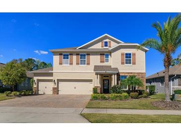 Two-story tan home with brick driveway, three-car garage, stone accents, manicured lawn, and lovely landscaping at 5142 Sage Cedar Pl, Sanford, FL 32771