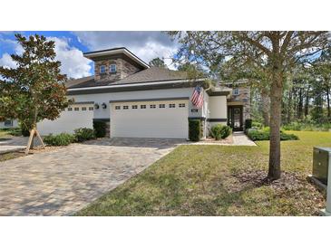 Charming home featuring a brick driveway, two-car garage, manicured lawn, and an American flag displayed on the front at 842 Aldenham Ln, Ormond Beach, FL 32174