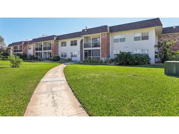 A view of the condo complex exterior with manicured lawn and concrete sidewalk leading to the building at 3800 Saxon Dr # 19B, New Smyrna Beach, FL 32169