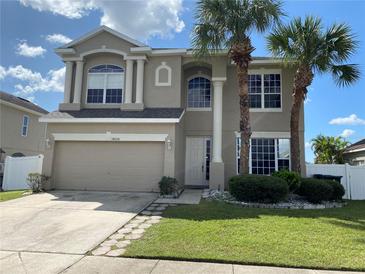 Beige two-story home with arched windows, neutral trim, a two-car garage and mature landscaping at 14020 Sanibel Isle Dr, Orlando, FL 32824