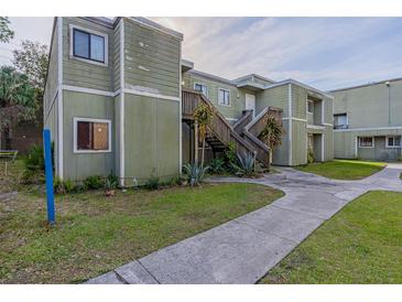 A weathered two-story exterior with a concrete walkway, lawn, and wood stairs that lead to the front door at 101 Scottsdale Sq # 101, Winter Park, FL 32792
