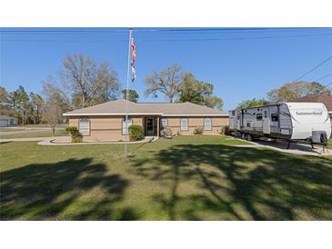 Single-story tan home with a well manicured lawn, American flag, and camper parked in the driveway at 5347 Pecan Rd, Ocala, FL 34472