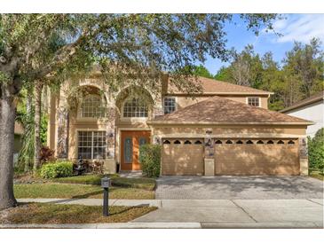 Inviting tan two-story home featuring a three-car garage, stone accents, manicured lawn, and mature trees at 2162 Camel Lake Ct, Oviedo, FL 32765