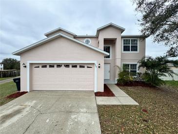 Two-story home featuring a two car garage, well-maintained landscaping, and a light pink exterior paint at 607 Kissimmee Ln, Kissimmee, FL 34759