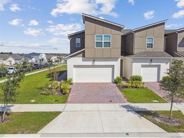 Modern townhome boasts a brick-paved driveway, a two-car garage, and well-maintained landscaping at 1195 Boardwalk Pl, Kissimmee, FL 34747