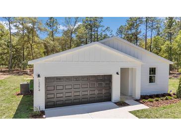 Charming white home showcasing modern architecture, a dark garage door and well-maintained landscaping at 13274 Sw 82Nd Ln, Dunnellon, FL 34432