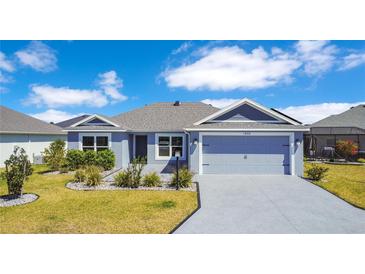 Charming single-story home features a two-car garage, manicured lawn, and beautiful landscaping under a bright sky at 1959 Keel Ct, The Villages, FL 34762