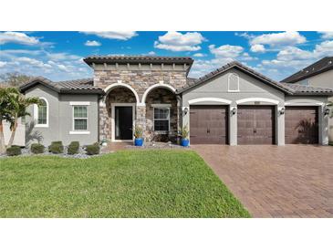Beautiful home showcasing a stone facade, a three-car garage, and a well-manicured front lawn at 4419 Liberty Bell Cv, Orlando, FL 32817