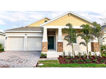 Charming home featuring a two-car garage, well-manicured landscaping, and a welcoming front entrance with stone accents at 1883 Blissful Dr, Kissimmee, FL 34744