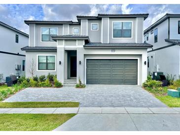 Modern two-story home featuring a gray brick driveway, lush landscaping, and an attached two-car garage at 10012 Voyager Way, Orlando, FL 32821