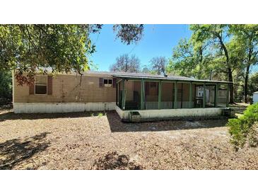 Side view of a single-story home featuring a large screened-in porch under a clear, blue sky at 20144 Se 156Th St, Umatilla, FL 32784