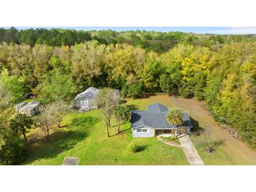 Aerial view of a charming single-story home with a gray roof, set on a lush green lawn surrounded by mature trees at 20639 Sw Rainbow Lakes Blvd, Dunnellon, FL 34431