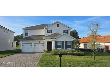 Charming two-story home showcasing a well-manicured lawn, brick driveway, and two-car garage, set against a blue sky at 18410 Blue Heron Cir, Deer Island, FL 32778