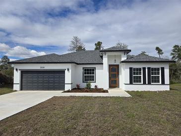 Charming home featuring a gray roof, gray garage door, modern front door, and a well-manicured lawn at 3519 Sw 131St Place St, Ocala, FL 34473