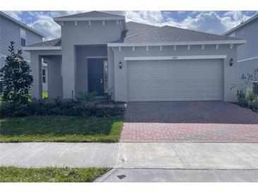 Charming single-Gathering home featuring a two-car garage, well-manicured lawn, and brick paver driveway at 1009 Hendon Loop, Davenport, FL 33837