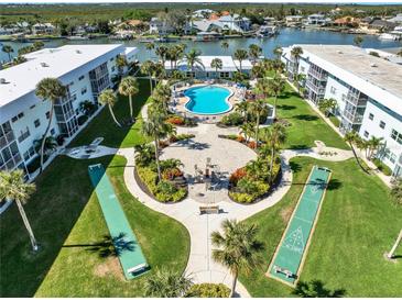 Aerial view showcasing a community with a pool, shuffleboard courts, and fire pit amidst lush landscaping and waterfront access at 325 N Causeway # 2080, New Smyrna Beach, FL 32169