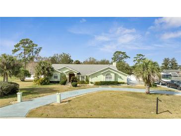 Charming single-story home with well-manicured lawn, mature trees, and a long driveway leading to the attached garage at 5170 Ne 64Th Ave, Silver Springs, FL 34488