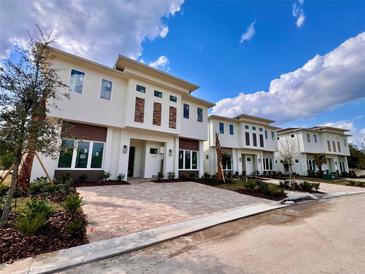 Modern townhomes featuring brick accents, paver driveways and professional landscaping under a bright blue cloudy sky at 7638 Whitemarsh N Way, Kissimmee, FL 34747