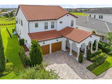 An exterior view of a two-story white house, featuring a terracotta tile roof, manicured landscaping, and a brick driveway at 8025 Topsail Pl, Winter Garden, FL 34787