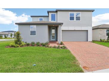 Charming two-story home with a well-manicured lawn and a brick driveway leading to the garage at 2933 Wild Olive Dr, St Cloud, FL 34772