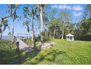 Lush backyard featuring a dock on the water, verdant lawn, trees, and a charming white gazebo at 703 Valencia Shores Dr, Winter Garden, FL 34787