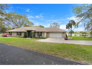 Charming single story home featuring a well-manicured lawn, mature trees, and a long driveway leading to an attached two car garage at 40610 Babb Rd, Umatilla, FL 32784