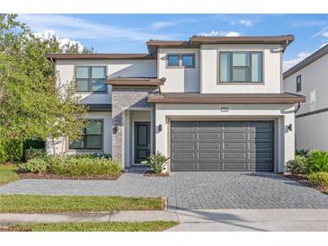 Two story home featuring a paved driveway, two car garage, stone accents, and manicured landscaping at 1205 Butterfly Orchid Rd, Davenport, FL 33837