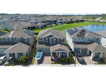 Aerial view of a two-story home with a manicured lawn in a lakeside community with solar panels on several houses at 10732 Petrillo Way, Winter Garden, FL 34787
