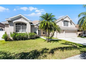 Inviting front yard featuring a well-maintained lawn, mature palm trees, and an attached two-car garage at 14136 Magnolia Glen Cir, Orlando, FL 32828