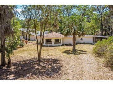 Exterior view of a white home featuring a distinctive round sunroom and a natural landscape with mature trees at 450 Cassady St, Umatilla, FL 32784