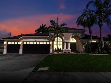 Beautiful home exterior featuring a three-car garage, well-manicured lawn, and mature palm trees against a colorful sunset sky at 814 Chamberlin Trl, St Cloud, FL 34772