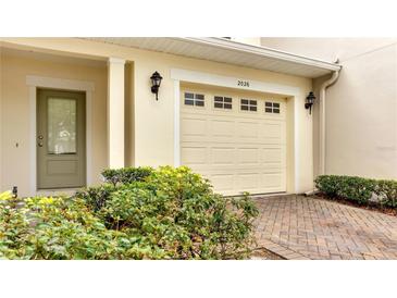 Beige home featuring a front entry garage with brick paver driveway and a well-maintained landscaped area at 2026 Cypress Bay Blvd, Kissimmee, FL 34743