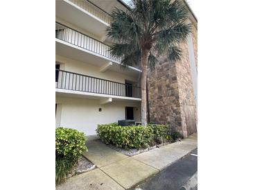 A condo exterior featuring a well-maintained facade, balcony, stone accents, and attractive landscaping with a mature palm tree at 2037 San Marcos Se Dr # 217, Winter Haven, FL 33880