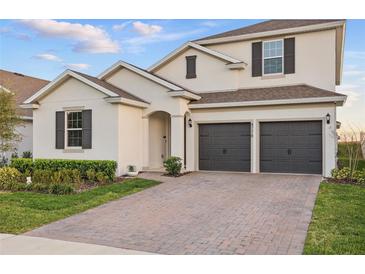 Two-story home with a two-car garage, brick driveway, manicured landscaping, and neutral exterior at 4778 Cragmere Loop, Clermont, FL 34711