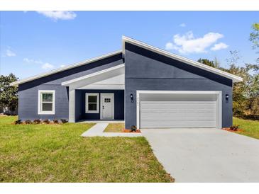 Contemporary blue home featuring a two-car garage, crisp white trim, and well-maintained lawn at 4761 Sw 142Nd Place Rd, Ocala, FL 34473