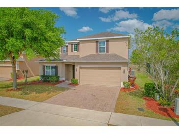 Charming two-story home with a manicured lawn, brick driveway, and attached two-car garage at 1040 Andalusia Loop, Davenport, FL 33837