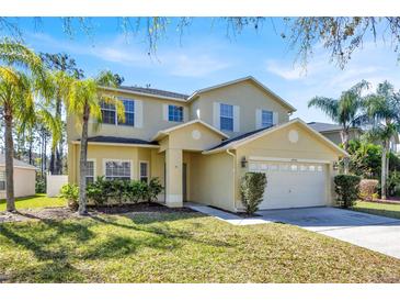 Two-story home featuring a two-car garage, a well-manicured lawn, and lush landscaping at 14740 Hartford Run Dr, Orlando, FL 32828