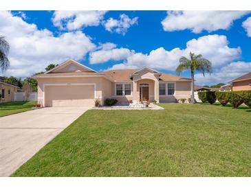 Charming single-story home features a manicured lawn, two-car garage, and inviting front entrance under a sunny, cloudy sky at 2712 Pearl Court, Kissimmee, FL 34743