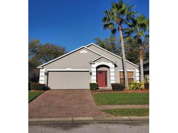 Charming home features a red front door, brick driveway, gray siding, and well-maintained landscaping with palm trees at 1457 Waukon Cir, Casselberry, FL 32707