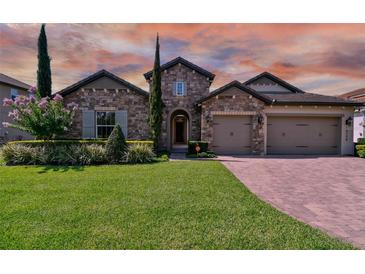 Beautiful stone home featuring a manicured lawn, tasteful landscaping, and a convenient three-car garage at 16736 Broadwater Ave, Winter Garden, FL 34787