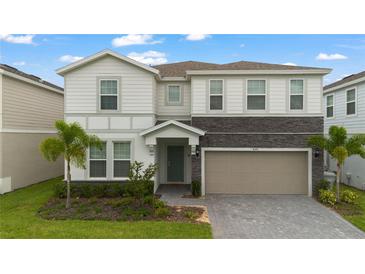 Charming two-story home with a stone accent, a gray-tone garage door and a landscaped front yard with palm trees at 4321 Lana Avenue, Davenport, FL 33897