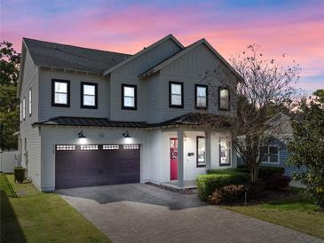 Charming two-story home with a brick driveway, attached garage, red door, and beautiful landscaping at 2108 Delaney Ave, Orlando, FL 32806