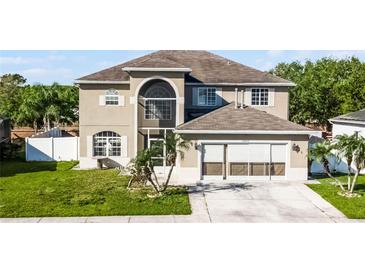 Beige two story home with a front yard, two-car garage, and arched windows at 5456 Crepe Myrtle Cir, Kissimmee, FL 34758