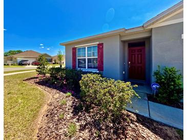 Charming single-story home featuring a red front door, tidy landscaping, and a well-manicured lawn at 992 Serchio St, Haines City, FL 33844