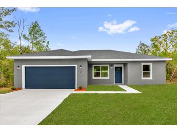 Charming single-story home featuring a well-manicured lawn, a blue door, and a two-car garage, offering great curb appeal at 23 Fisher Run, Ocklawaha, FL 32179