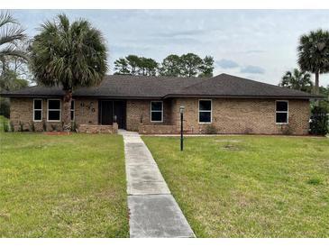 Charming brick home with a well-manicured lawn, walkway, and mature palm trees at 635 Malaga Ave, Deltona, FL 32725