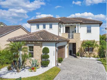 Stunning two-story home featuring a tile roof, stone accents, a paver driveway, and lush landscaping at 9888 Mere Pkwy, Orlando, FL 32832